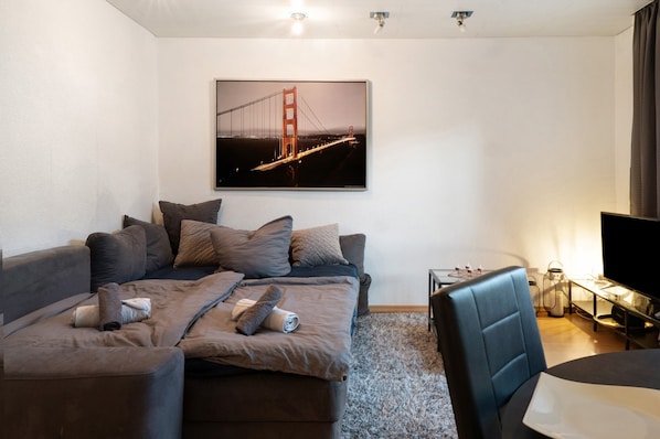 Un salon moderne avec un canapé, un téléviseur et un tableau encadré représentant un pont.