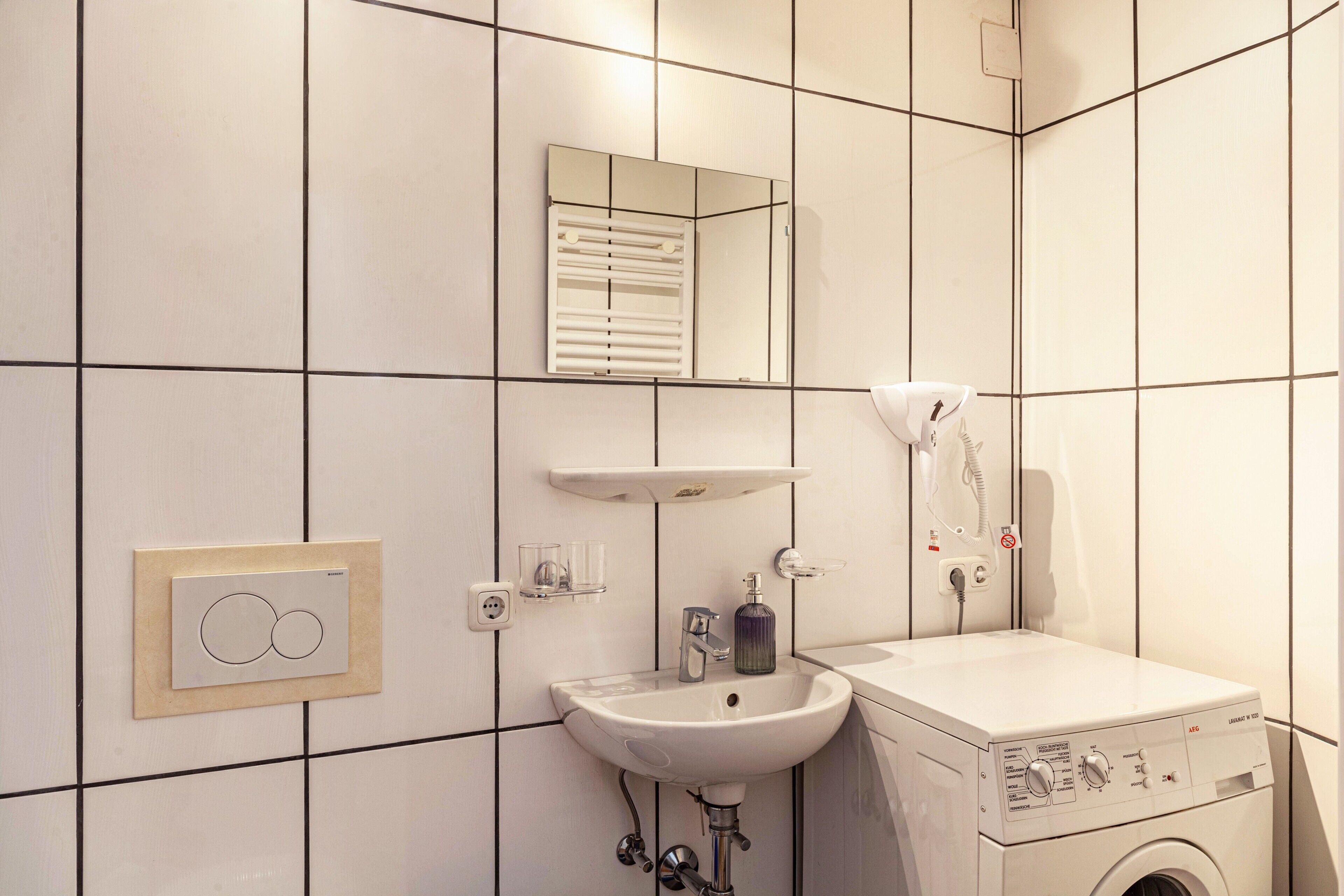 Een badkamer met een wastafel, spiegel, handdoekhouder en een wasmachine.