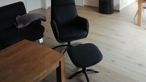 Una sala de estar con un sofá negro, una mesa de madera, una silla de oficina negra y una chimenea negra.