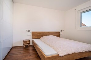 Une chambre avec un lit en bois, un petit tabouret en bois et une fenêtre.
