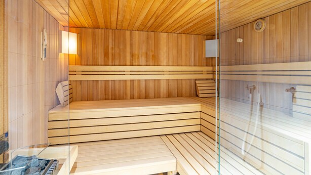 Een sauna met houten banken en een glazen scheiding, een klok en een boiler.