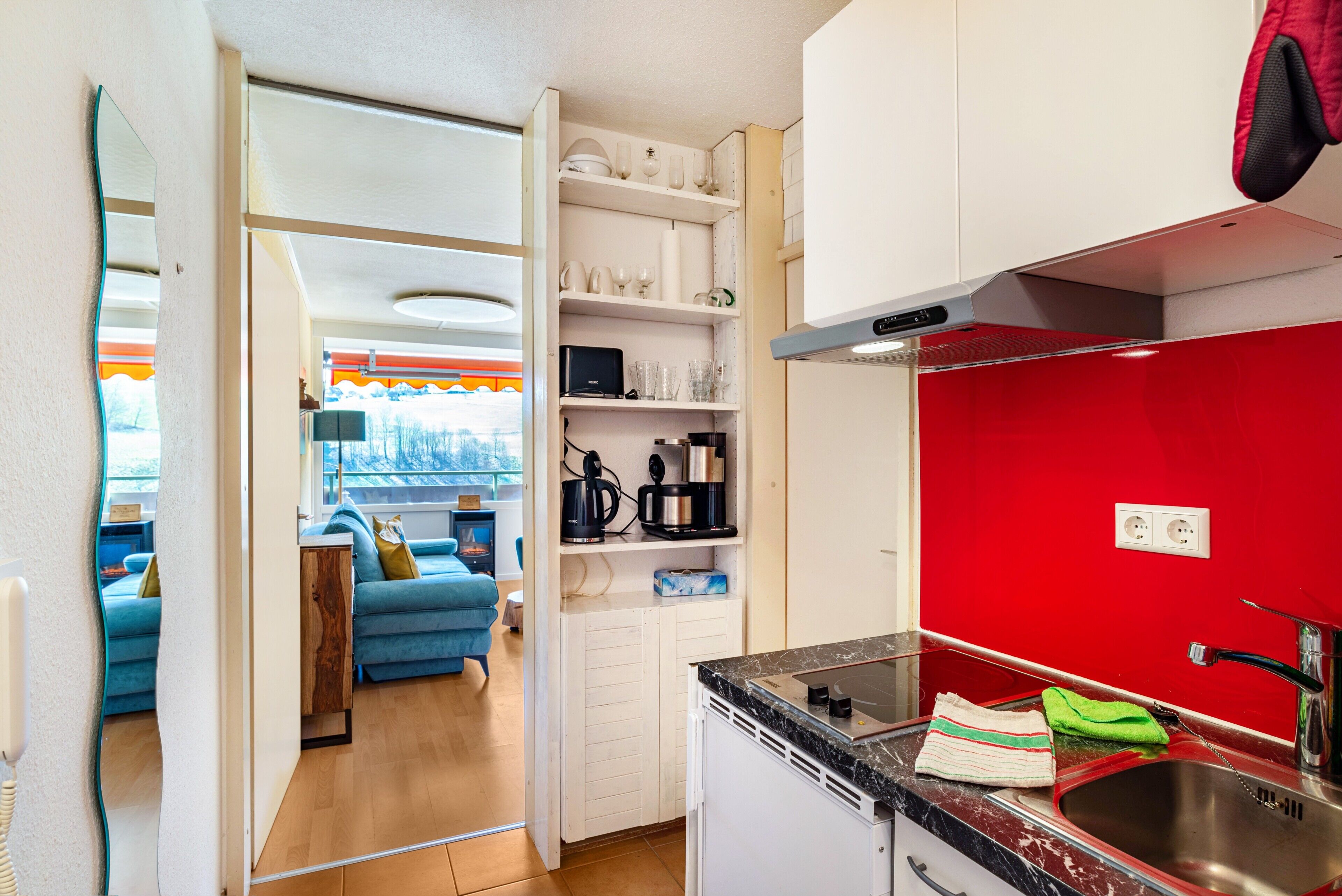 Eine kleine Küche mit roter Spritzschutzwand, einem eingebauten Backofen und einem Spülbecken.