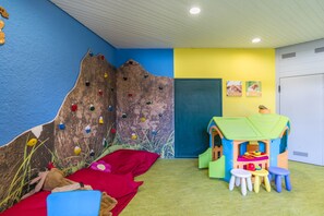 A children's playroom with a climbing wall, a playhouse, and a bed with toys.