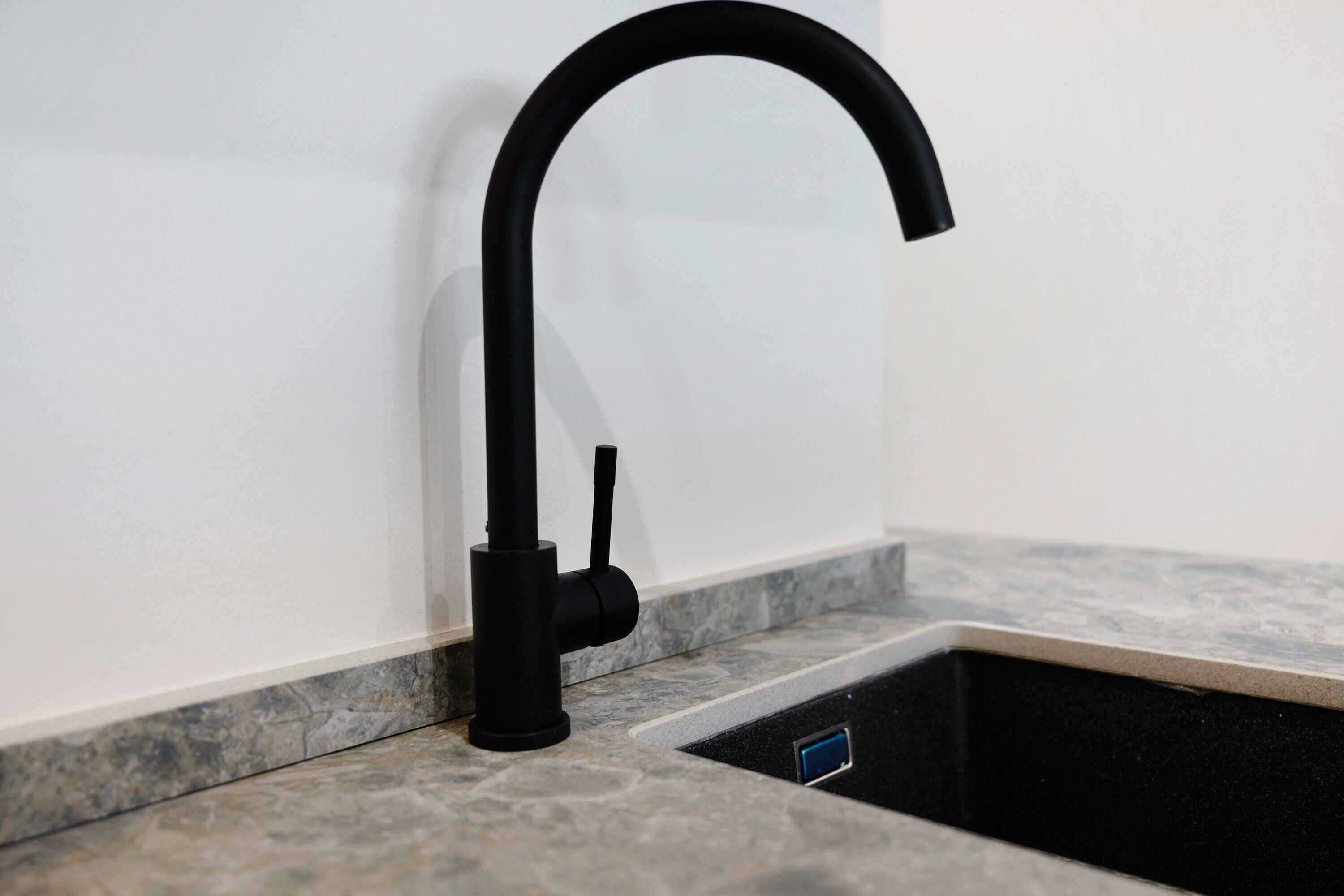 A kitchen sink with a black faucet, a marble countertop, and a black drain cover.