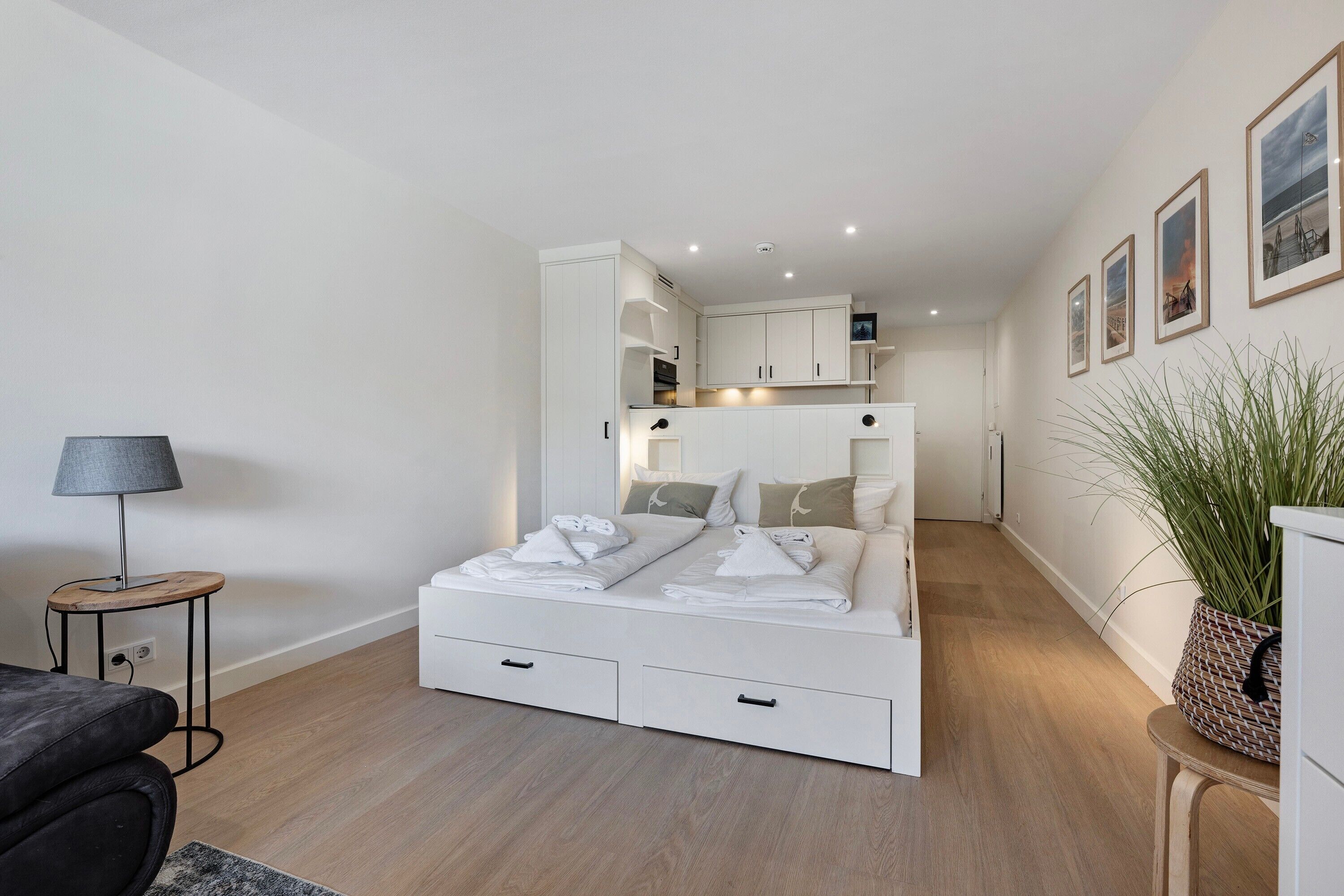 Ein modernes Schlafzimmer mit einem Bett, Nachttischen, einem kleinen Schreibtisch und einem Blumentopf.