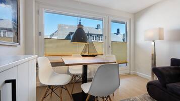 A dining area with a table, chairs, a pendant light, and a view through large windows.