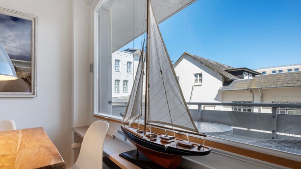A model sailboat on a windowsill, a white chair, and a table with a lamp.