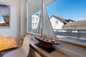 A model sailboat on a windowsill, a white chair, and a table with a lamp.