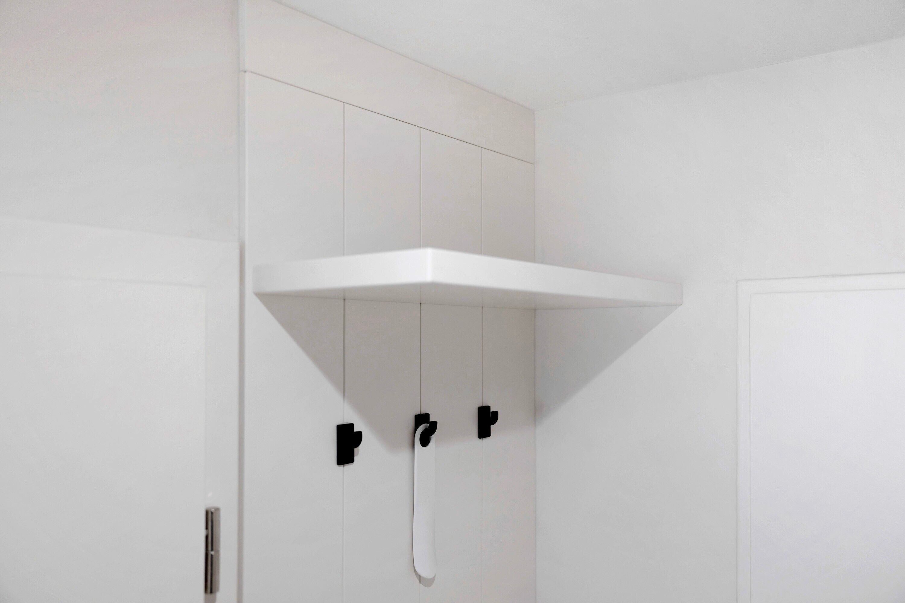 A white bathroom with a white shelf mounted on the wall, a towel rack, and a showerhead.