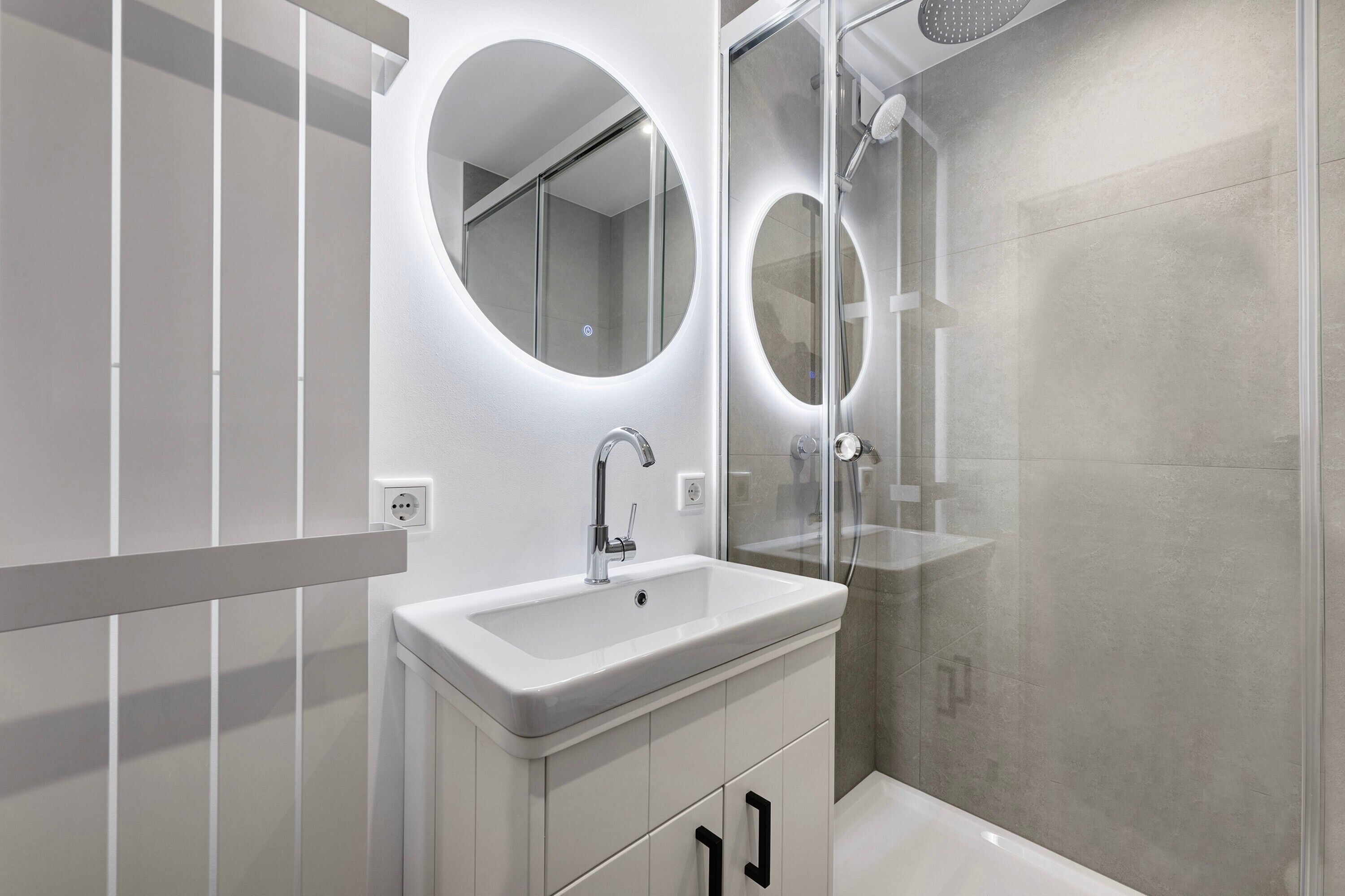 A modern bathroom with a white sink, mirror, and shower.