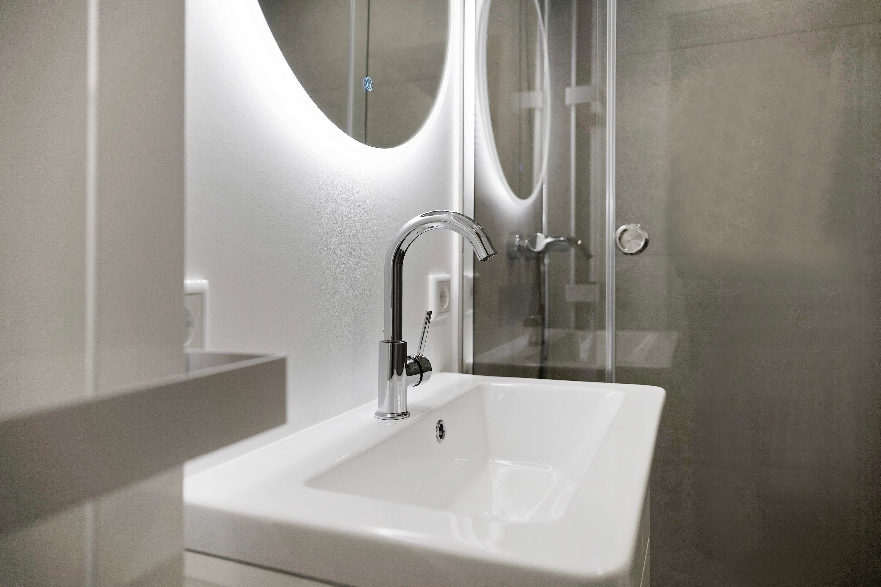 A modern bathroom with a white sink, chrome faucet, and a glass shower enclosure.