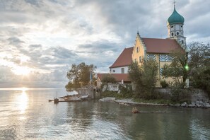 A historic building with a tower and a red roof by a calm body of water.