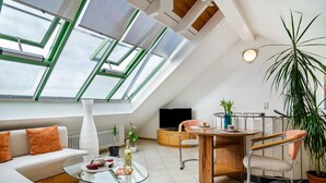 A modern loft-style room with a sloped ceiling, skylights, a glass coffee table, a sofa, a dining table, and a chair. - Holiday Apartment "Bodenseeblick" with Wi-Fi on Request (Meersburg)