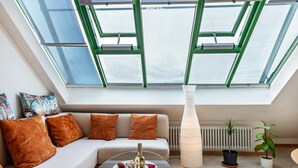 A modern living room with a glass ceiling, a sofa with brown cushions, a glass coffee table with a bottle and glasses, and two potted plants. - Holiday Apartment "Bodenseeblick" with Wi-Fi on Request (Meersburg)