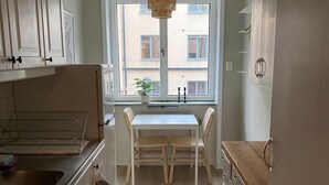 A kitchen with a white table and chairs, a window with a view of buildings, and a hanging light fixture.