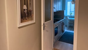 A hallway leading to a kitchen with a dining area, a framed picture on the wall, and a door with a textured panel.