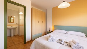 A hotel room with a bed, a nightstand, a mirror, a wardrobe, and a bathroom with a sink.