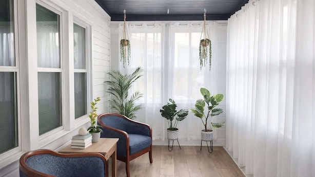 A sunroom with white walls, wooden flooring, two blue armchairs, a small table with books, and hanging plants. - The Heron House, King Bed Suite, *Spacious Remodeled House* (Joliet)