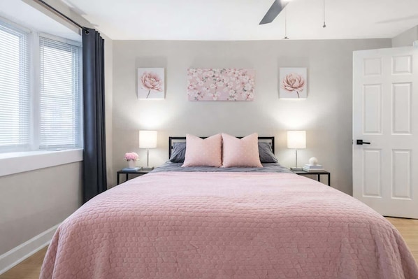 Un dormitorio con cama, dos mesitas de noche, una ventana con persianas y una puerta.