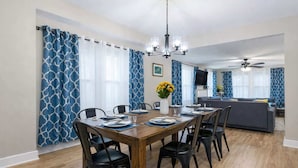 A dining area with a wooden table set for six, black chairs, a chandelier, and a sofa in the background. - The Heron House, King Bed Suite, *Spacious Remodeled House* (Joliet)