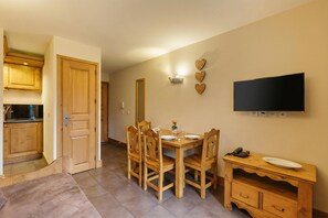 Uma área de refeições com uma mesa e cadeiras de madeira, uma TV na parede e um armário de madeira com um telefone e um prato.