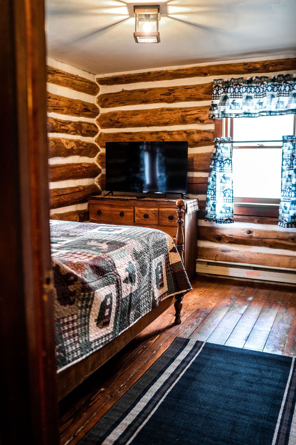 Un dormitorio de cabaña de madera con cama, cómoda y televisor de pantalla plana.
