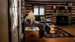 Ein gemütliches Blockhaus-Interieur mit Kamin, einer Couch, einer Lampe und einem Teppich.