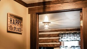 Ein Holzhütten-Interieur mit Deckenventilator, einem Bett mit Quilzdecke und einem an der Wand hängenden Schild mit der Aufschrift 'THE CABIN IS MY HAPPY PLACE'.