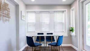 A room with a glass table and four blue chairs with gold legs, a window with blinds, and a plant on the windowsill. - Family/Pet-Friendly Riverside Home w/Amazing Views (Prospect)