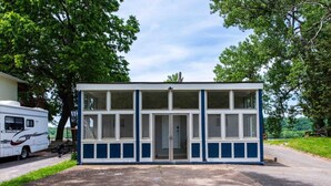 A small, single-story building with a central door and large windows, surrounded by trees and a parked RV. - Family/Pet-Friendly Riverside Home w/Amazing Views (Prospect)