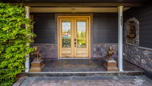 Ein dunkles Holzhaus mit einer Steinaußenseite, einer Doppeltür mit Glasscheiben und zwei Löwenstatuen auf der Veranda.