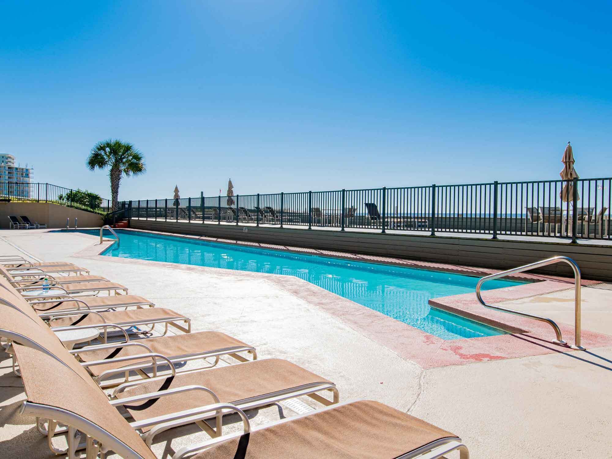 A pool area with lounge chairs and a view of the ocean.