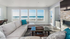 Una sala de estar moderna con un amplio ventanal con vistas a la playa, una chimenea y un espacio de estar acogedor.