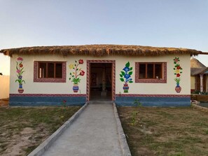 A traditional house with a thatched roof, colorful floral wall decorations, and a concrete pathway leading to the entrance.