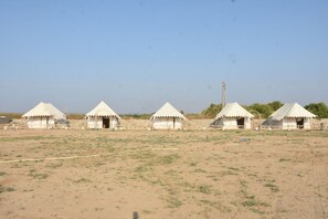 A row of white tents with a flat roof, set in a dry, grassy area.