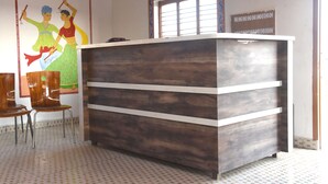 A reception desk with a wooden finish and white horizontal stripes, a tiled floor, and a colorful mural on the wall. - Ram Rann Resort (Bhachau)