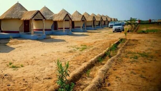 A row of thatched-roof huts with a dirt ground and a few cars parked nearby. - Ram Rann Resort (Bhachau)