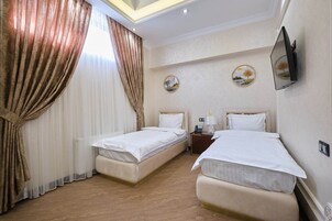 Habitación de hotel con dos camas, un televisor montado en la pared y una mesita con lámpara.