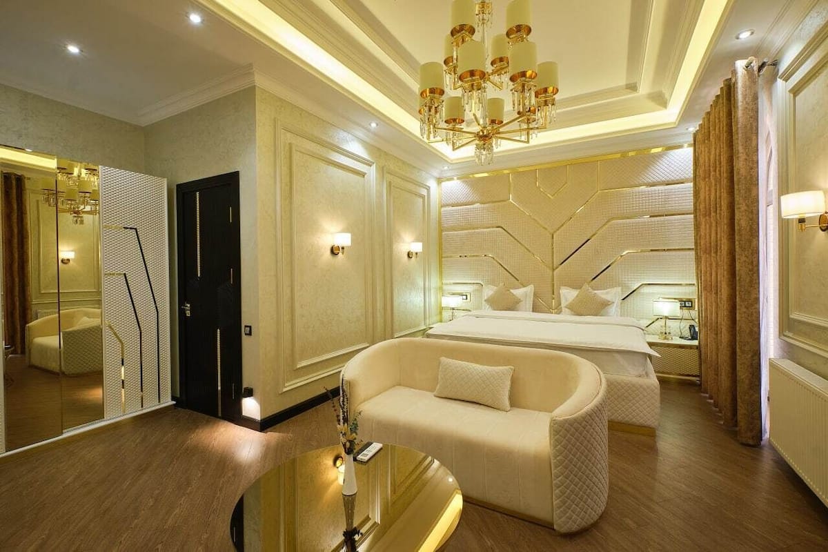 A hotel room with a large bed, a sofa, a mirror, and a chandelier.