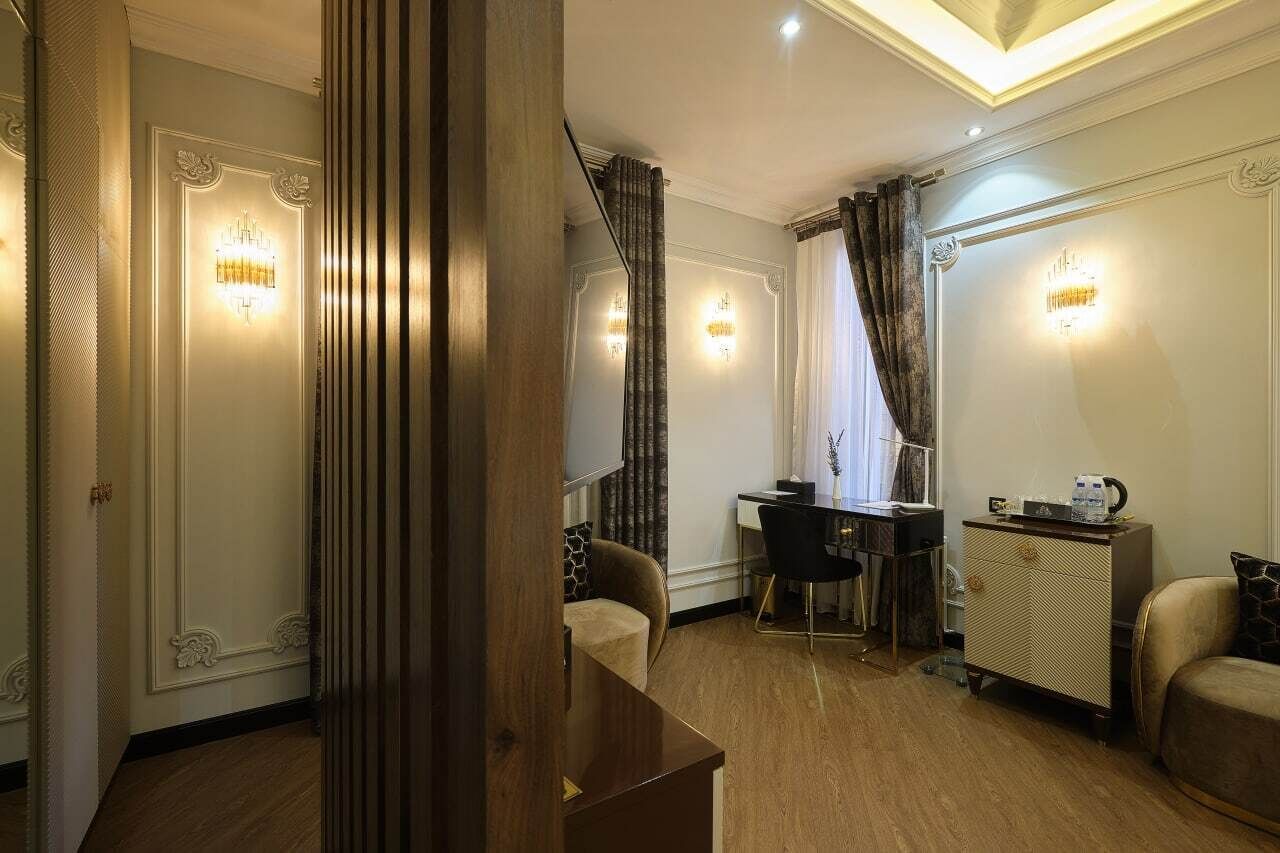 A hotel room with a wooden floor, a desk with a chair, a wardrobe, and a bed with a headboard.