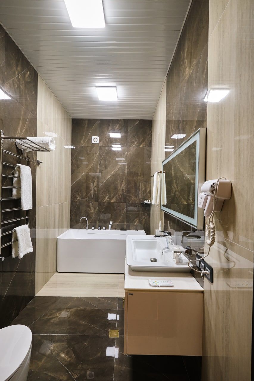 A modern bathroom with a bathtub, a vanity with a mirror, a hairdryer, and a towel rack.