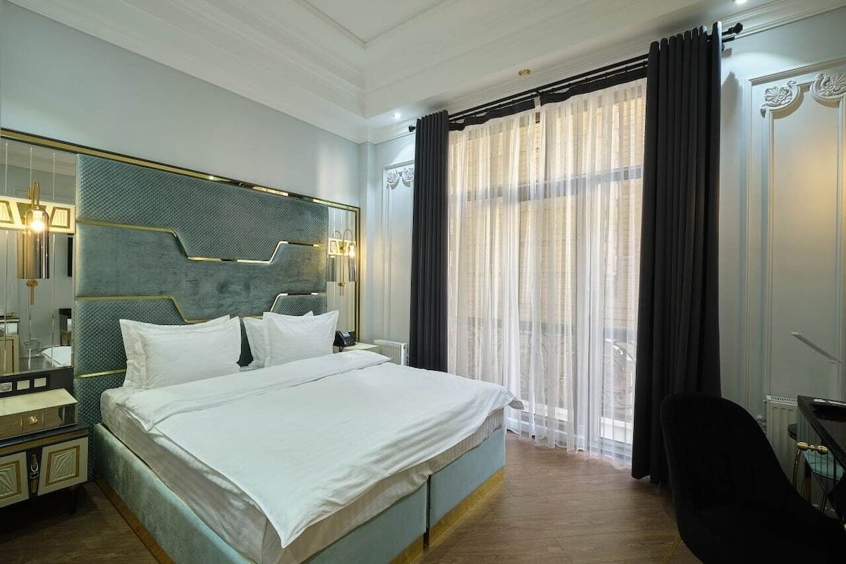 A hotel room with a large bed, a bedside table, a mirror, and a window with curtains.