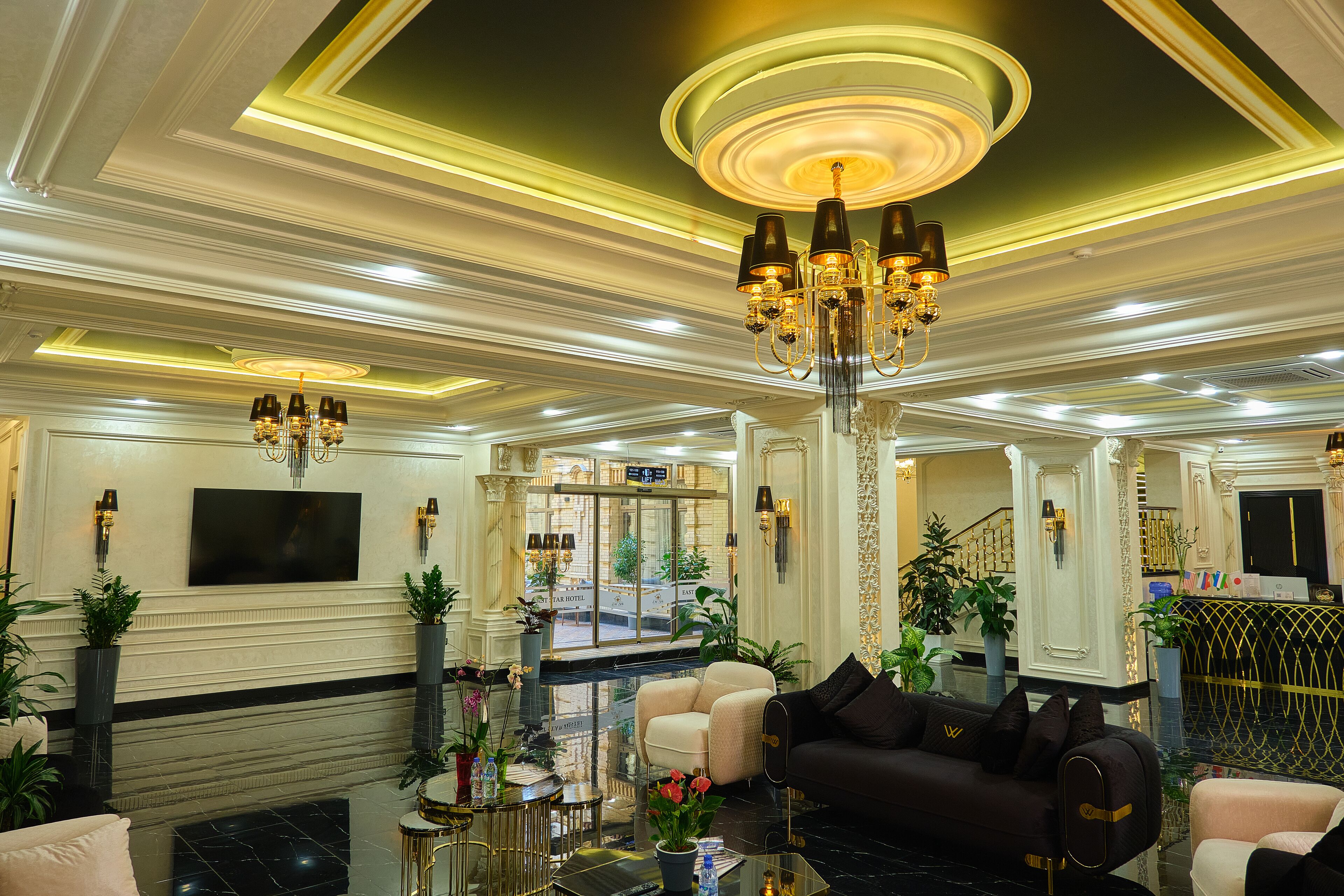 A luxurious lobby with a chandelier, sofas, a TV, and potted plants.