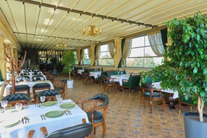 A restaurant with multiple tables set for dining, featuring green upholstered chairs and white tablecloths. - East Star Hotel (Samarkand)