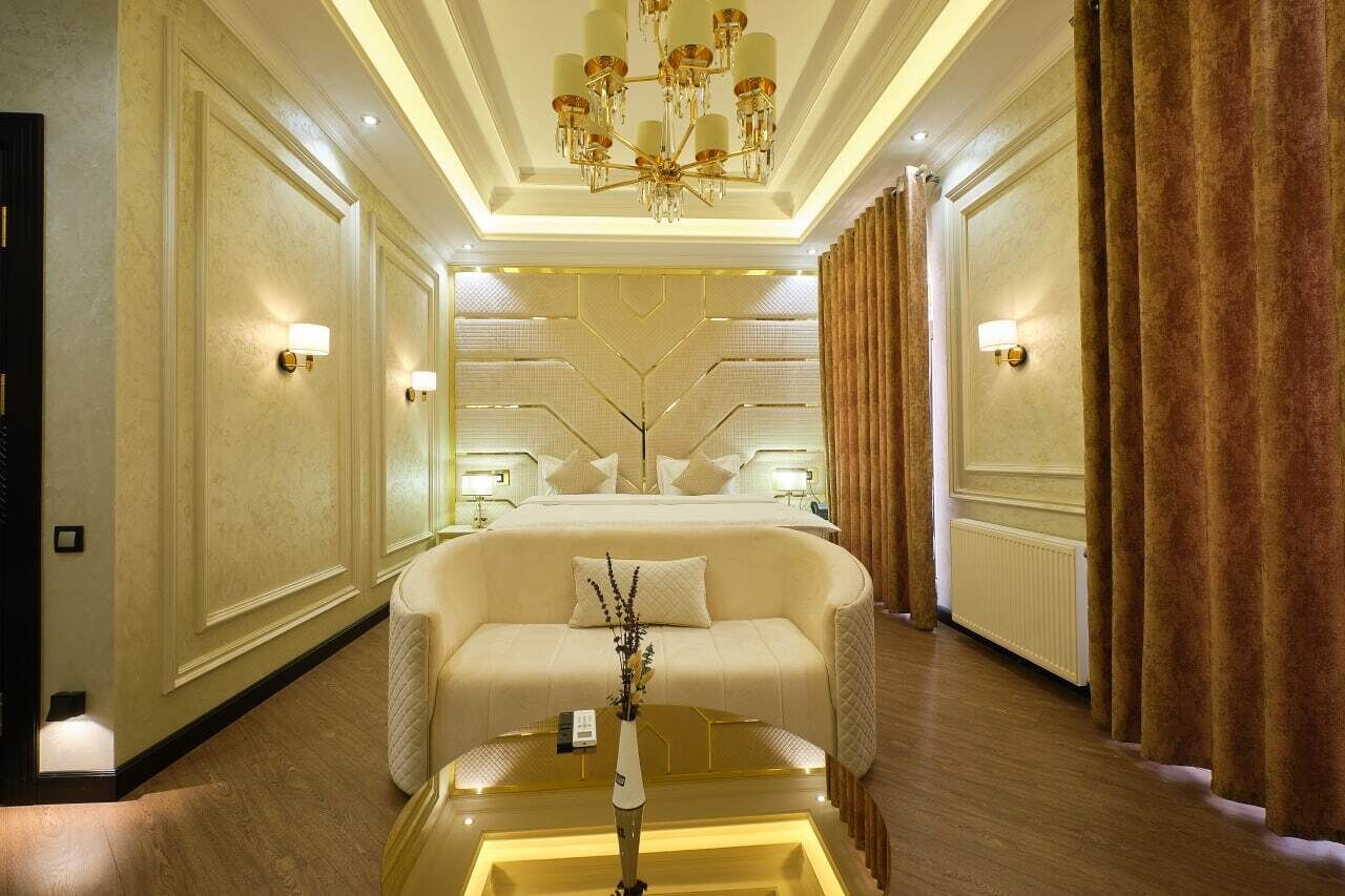 Una habitació d'hotel luxosa amb un llit gran, una zona de seients, un penjador de cristall i un ram de flors.
