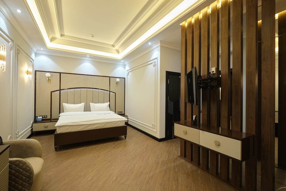 A modern hotel room with a large bed, bedside tables, a TV, and a wooden wardrobe.