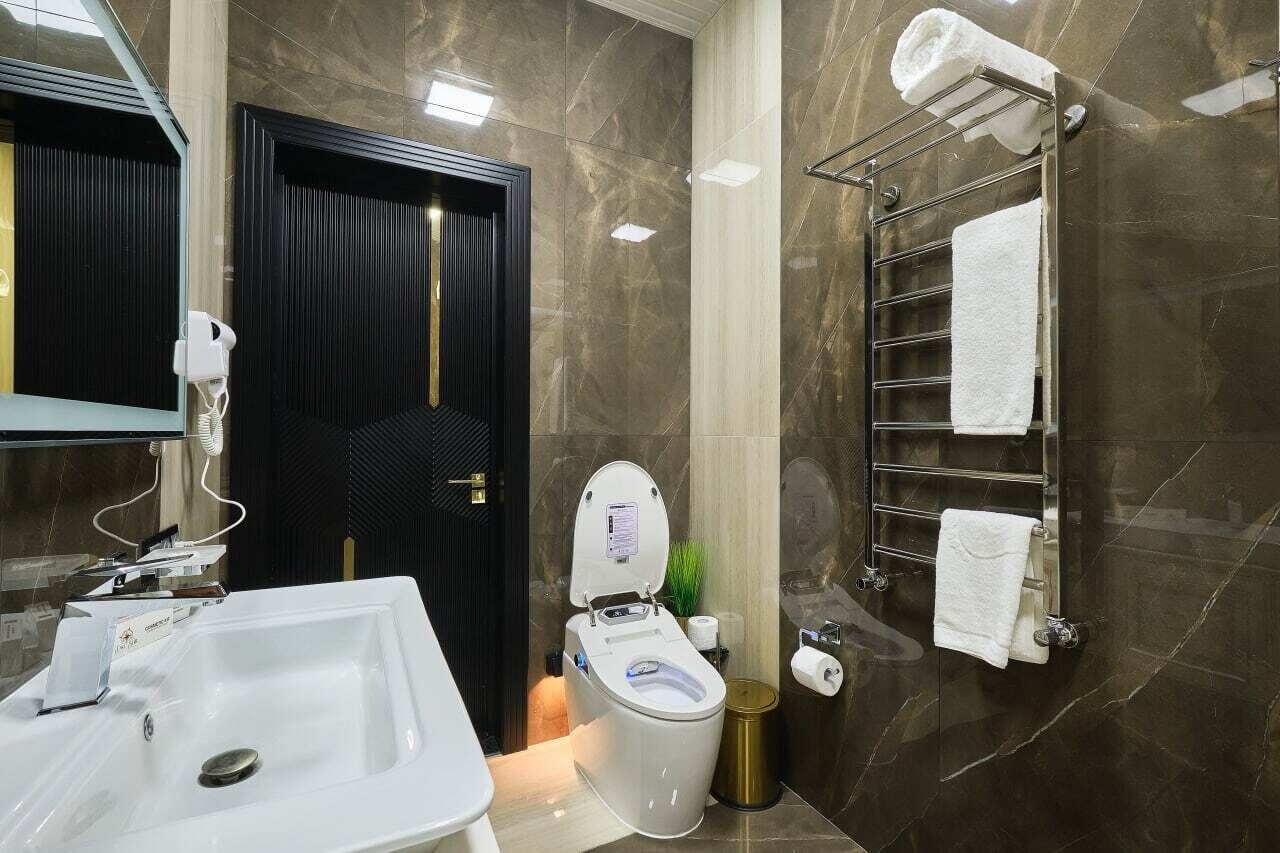 Un bagno moderno con lavandino bianco, un WC, un porta asciugamani e una porta nera.