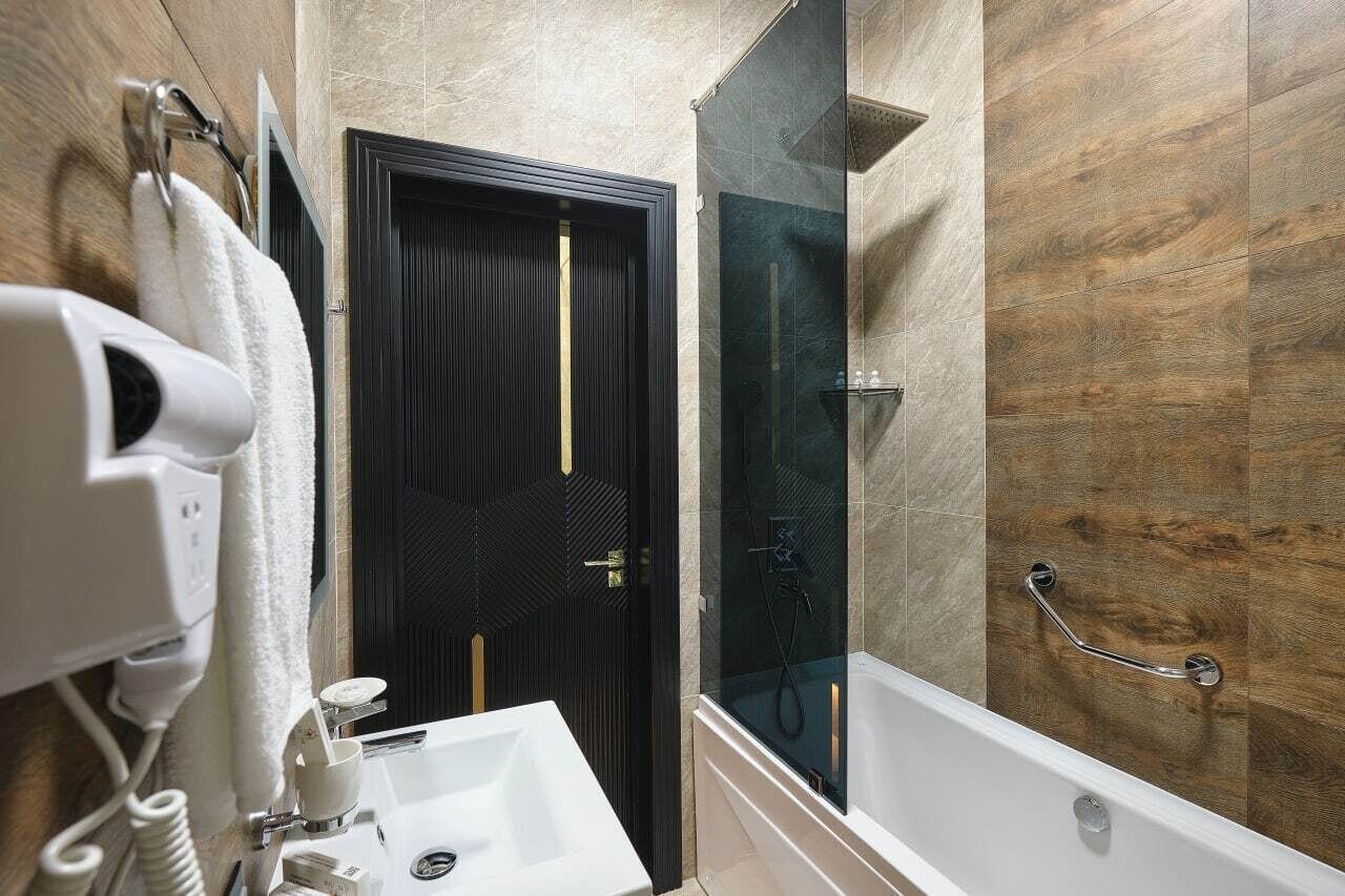 A modern bathroom with a dark wooden door, a glass shower enclosure, and a white sink.