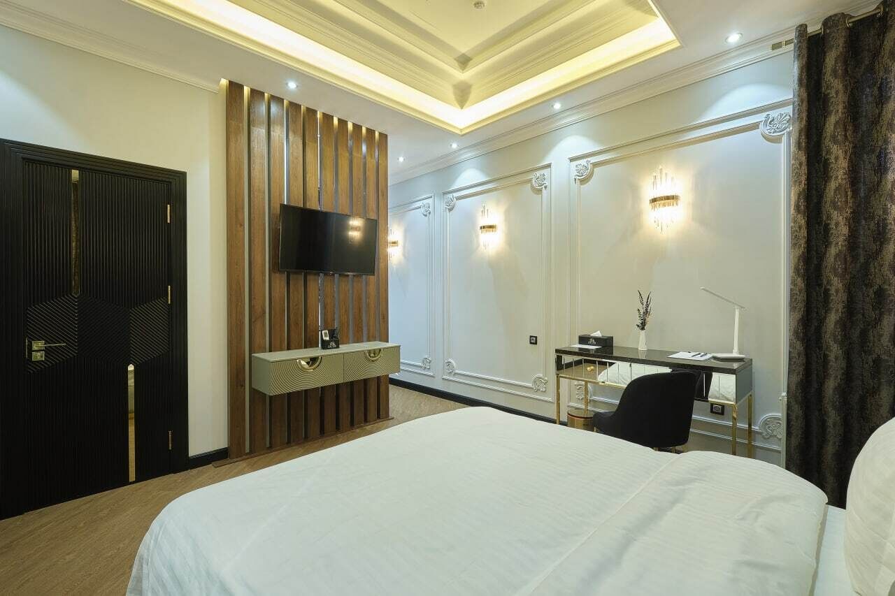 Ein Hotelzimmer mit einem großen Bett, einem Schreibtisch mit Stuhl, einem flachbildfernseher an einer Holzvertäfelung und einem Kleiderschrank mit Spiegel.