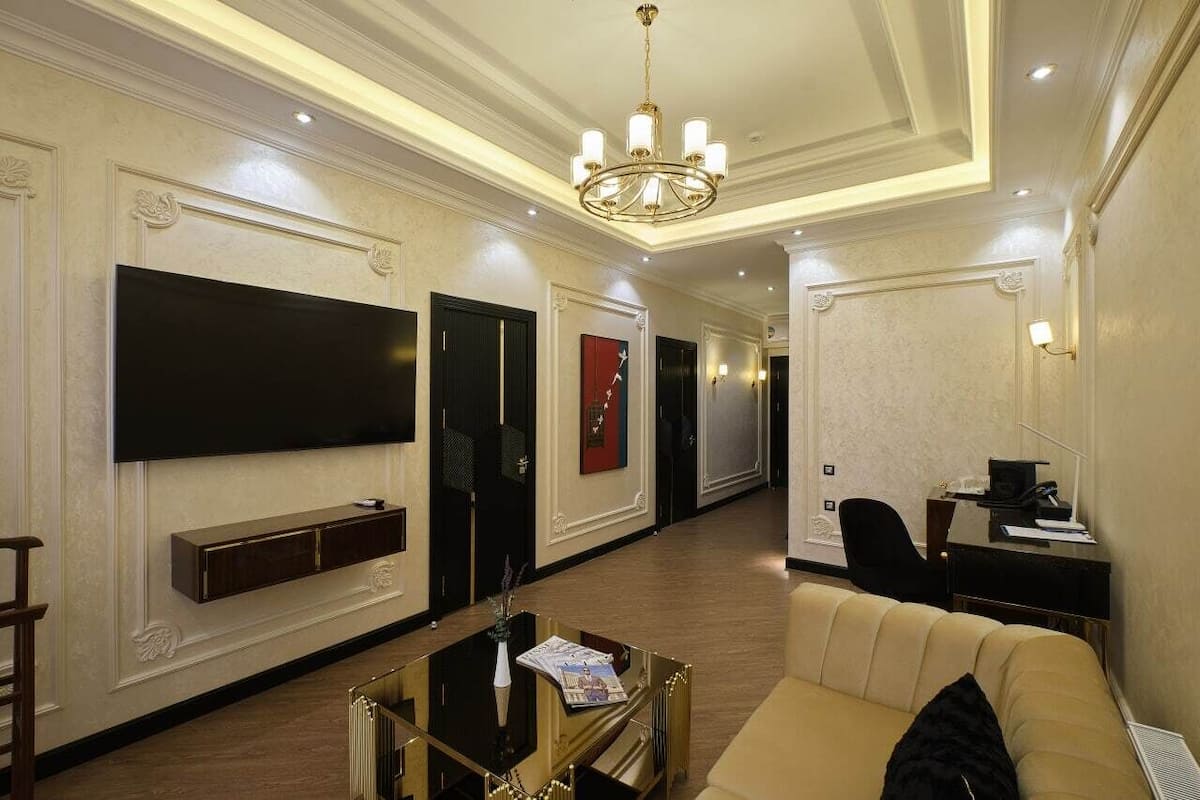 A hotel lobby with a large flat-screen TV, a sofa, a desk, and a chandelier.